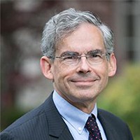 A man in a dark grey suit and grey hair with glasses.