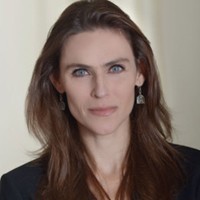 A head shot of a woman with long brown hair who is wearing earrings and a dark blazer and shirt