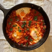 A photo of an iron skillet with eggs, tomato sauce, and some herbs in it.