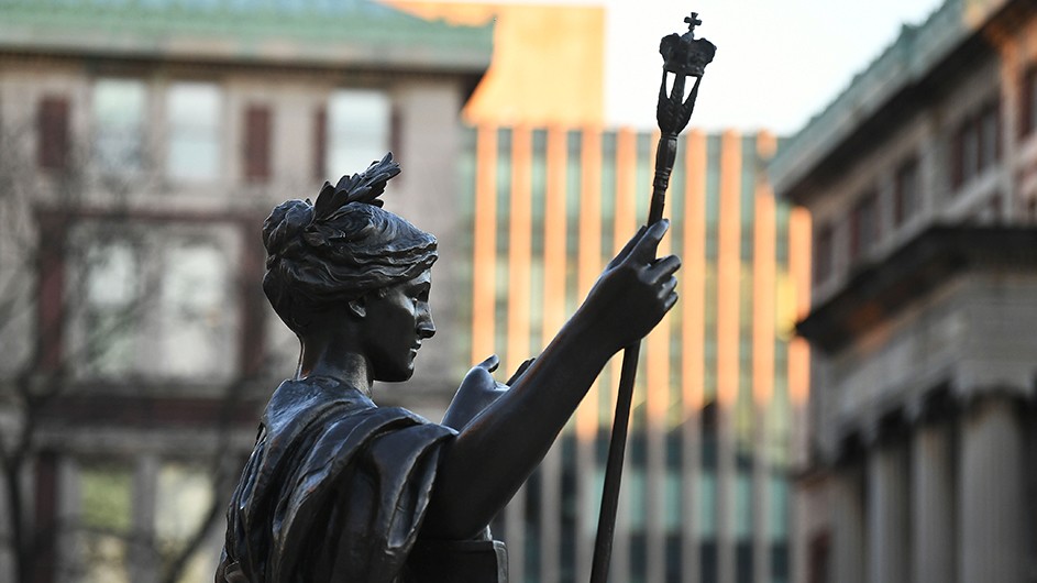 A close up of Alma Mater's profile with Philosophy Hall, Kent Hall, and the Law School in the background 