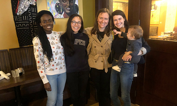 Four former roommates from Columbia and a baby pose together at a restaurant.