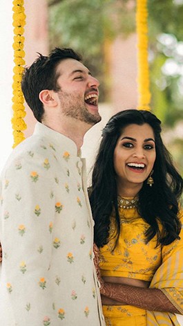 David and Sonali, in dhoti and sari, smile and laugh as they hug one another.