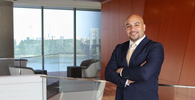 Photos by Nicole Pereira Michael Alberto standing with arms crossed in front of the Vagelos Building balcony with a view of the George Washington Bridge in the background.