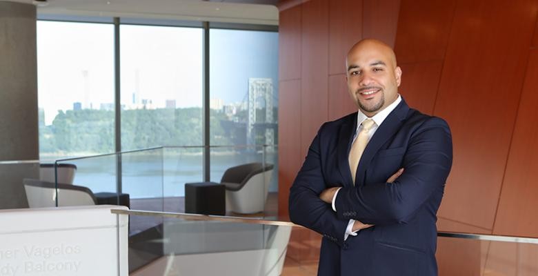 Michael Alberto standing with arms crossed in front of the Vagelos Building balcony with a view of the George Washington Bridge in the background.