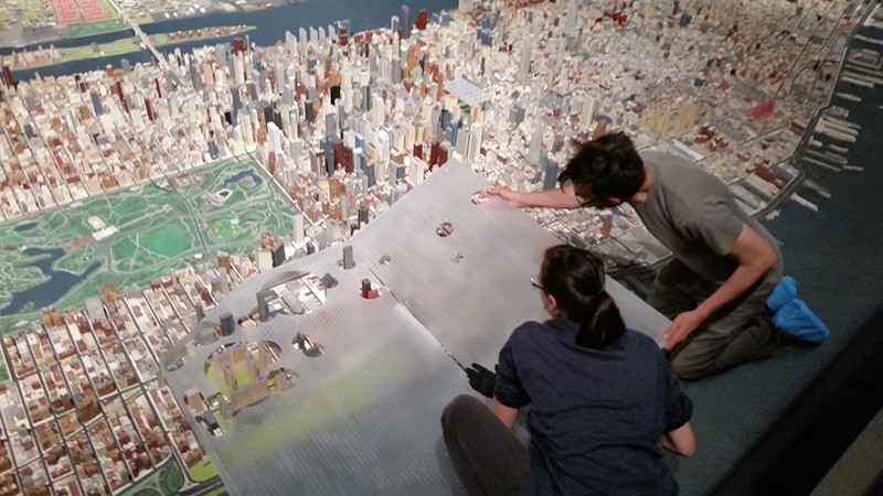 Queens Museum staff installs student models into the New York City Panorama for the Never Built New York exhibition. Photo by Josh Jordan Two people lean over a three-dimensional model of Manhattan