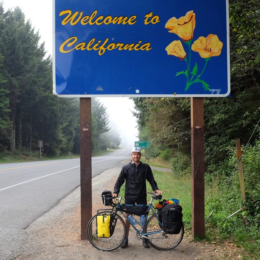 Man on a bike in front of a sign welcoming drivers to California