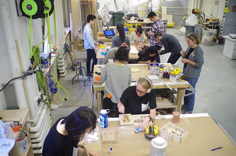 GSAPP students working in the Fab Lab on campus. Photo by Josh Jordan Men and women, sitting at and standing next to work tables, fashion materials and build models.