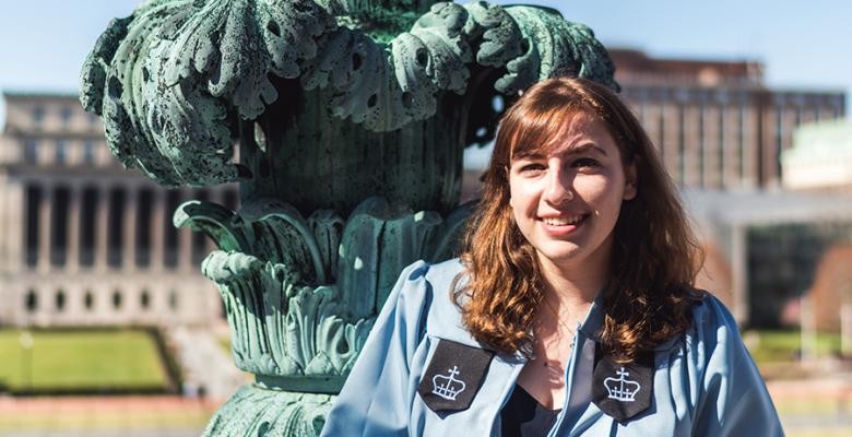 Sara Sakowitz in her Columbia baby blue graduation robe in front of a rusty green statue