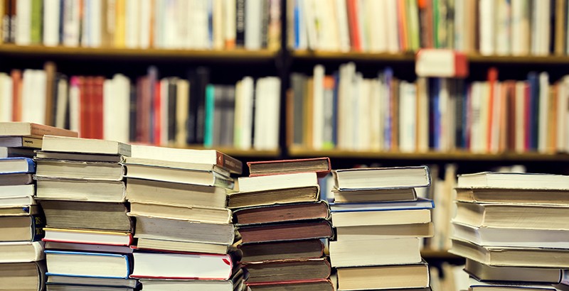 stacks of books in front of a shelf full of books