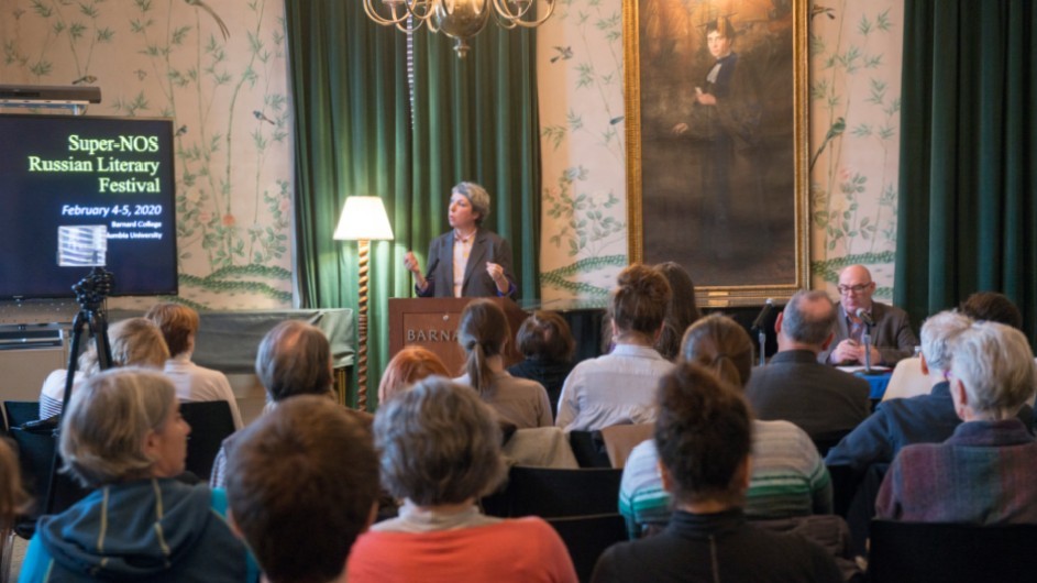 A woman speaking at the podium by a lit floor lamp in front of an audience