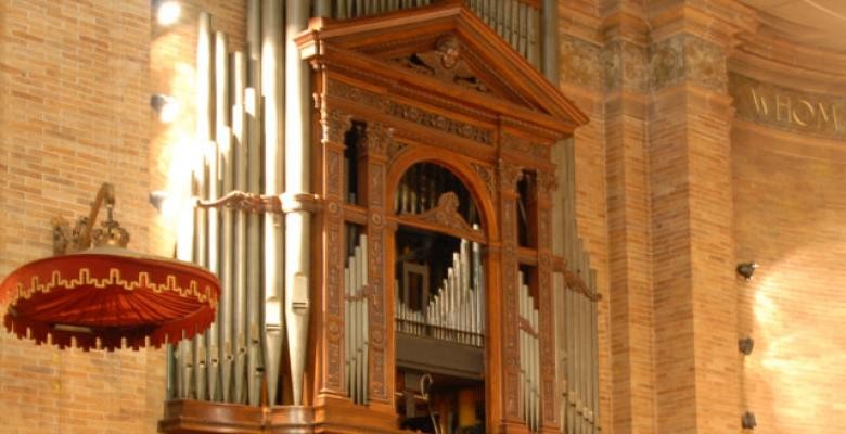 image of a tall light brown wooden organ with pipes alongside and in the rear of the organ 