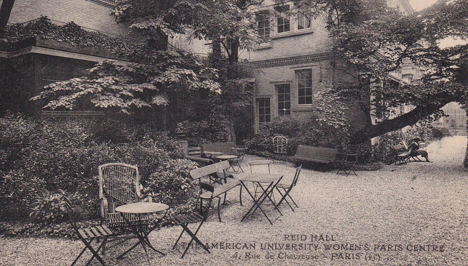 A black and white photograph of an 18th century building in a garden courtyard with benches. 