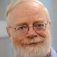 headshot of white haired man with beard and wire frame glasses