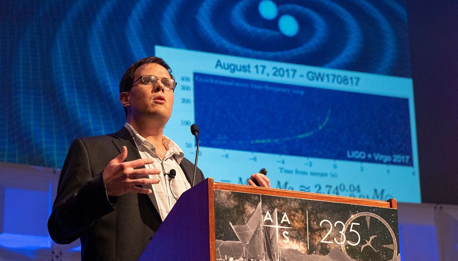 Brian Metzger delivers a presentation on his research at the 235th American Astronomical Society meeting. Photo: Courtesy of AAS man with glasses brown hair in sports jacket next to blue powerpoint addressing a group