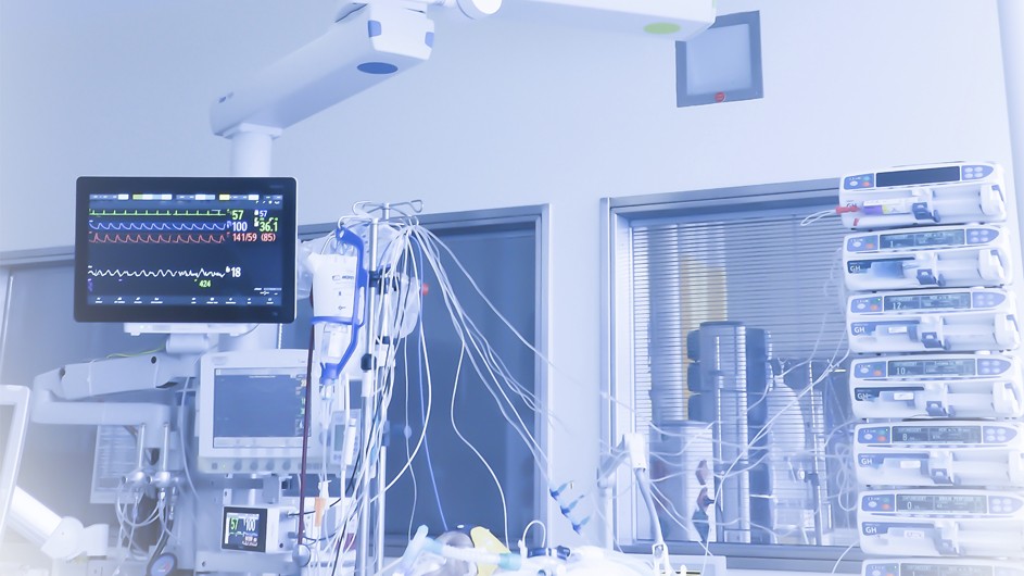 Intensive Care Unit with raised computer screen with squiggly data lines, lab supplies on desk, computer and IV with lots of wires, image tinted light blue