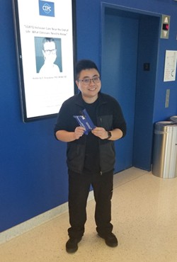 Justin Tsui, young man with black hair and glasses, holding a blue pouch