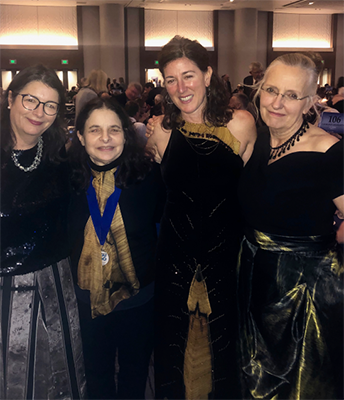 Four women in row with formal gowns, three brown hair and one with grey