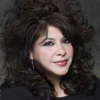 Angela M. Christiano Angela M. Christiano: A woman with long curly black hair staring into the camera.