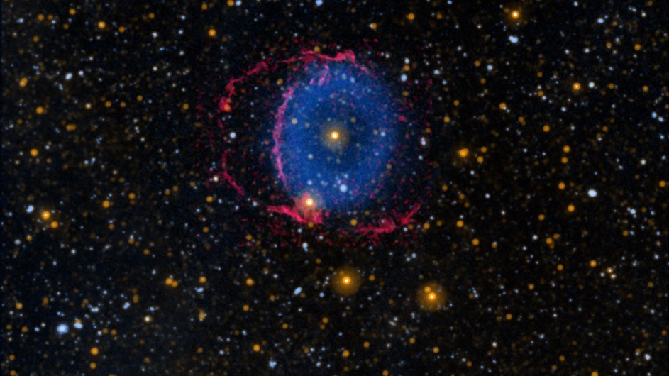 Black sky with hundreds of small stars and at center a blue donut-shaped ring with red lines surrounding it