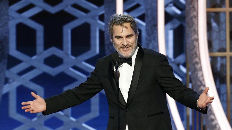 Middle-aged man with grey hair and beard smiling wearing black and white tux. Hands opened wide. Against light blue background