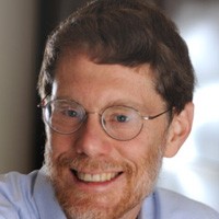 Andrew Millis: A brown haired man with round glasses and a brown beard staring into the camera.