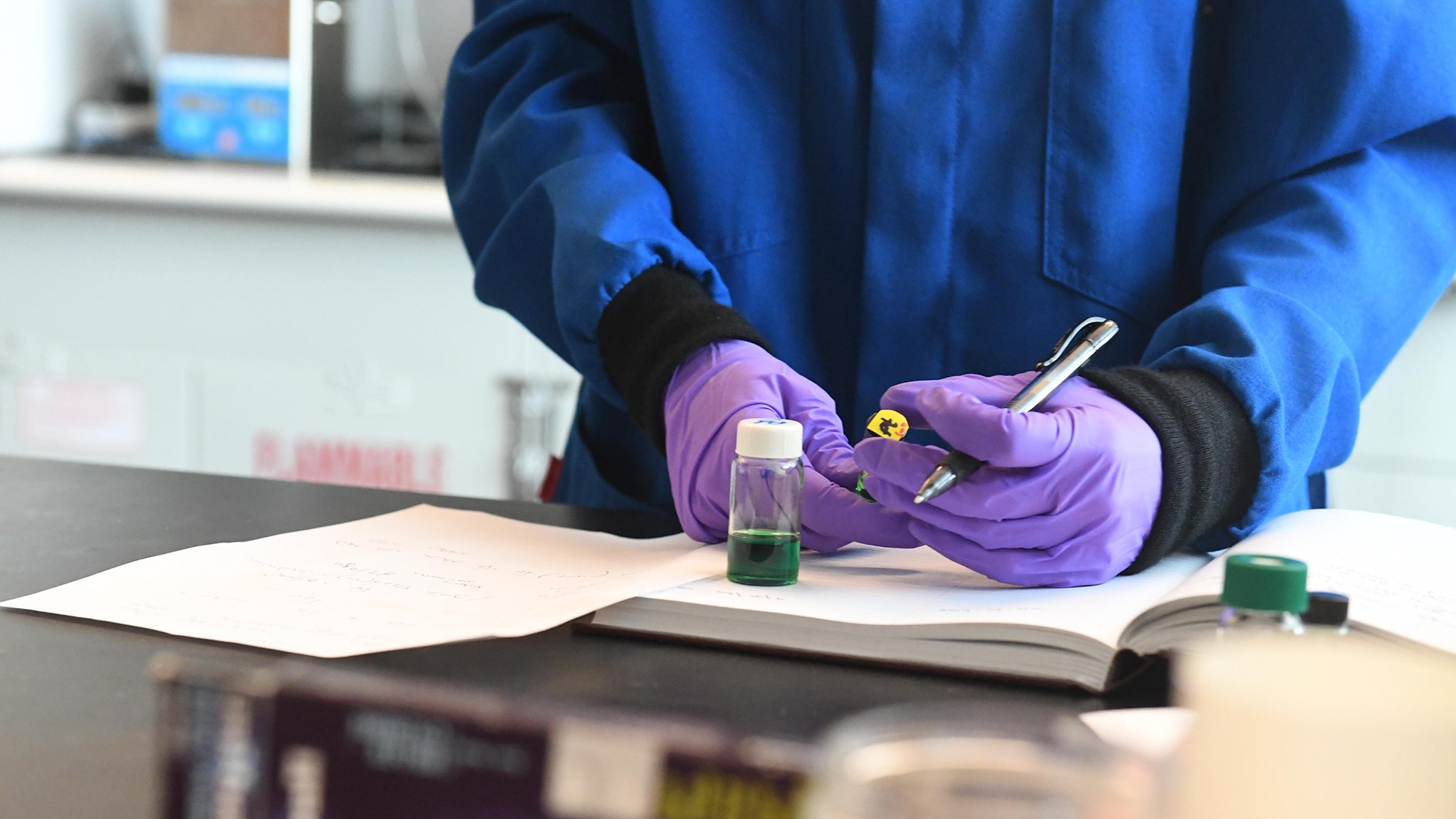 Bottom half of person with blue coat and purple gloves writing a notation in a notebook