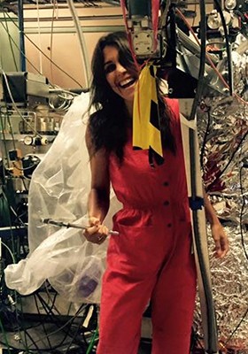 Theanne Schiros is a materials scientist who reimagines textiles through technology, biology and sustainable design. Woman in red pants suit with long, brown hair stands amid machinery