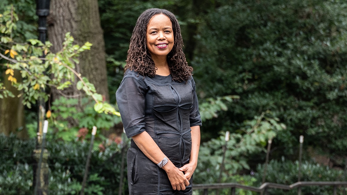 woman in black dress standing in a leafy park.