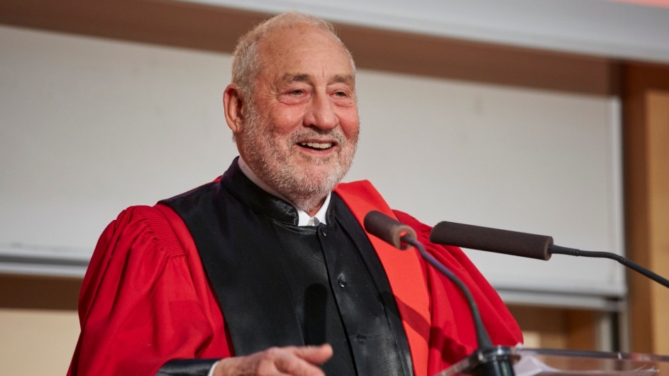 University Professor Joseph E. Stiglitz has had a busy year, traveling around the world talking about progressive economics, the new era of globalization and the impact of technology on social and political realities. Joseph Stiglitz: a man with gray hair in black and red academic robes, smiling behind a podium