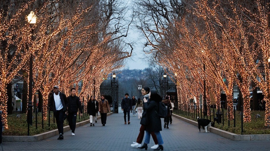 Students walking along College Walk at Columbia during the winter when the trees are lit up.
