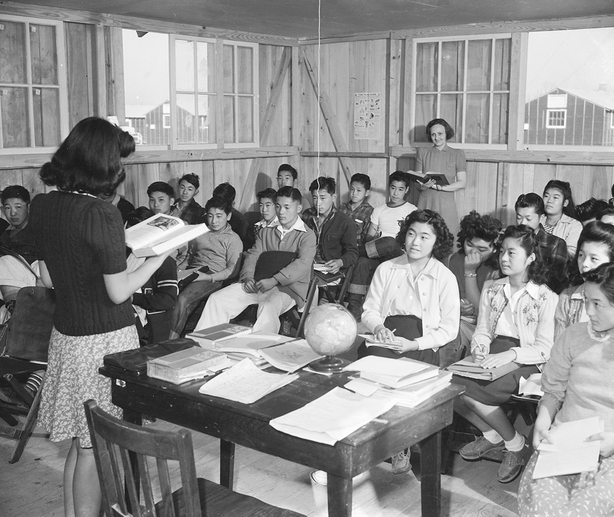"Mrs. Ziegler oversees her ninth-grade class at the internment camp in Jerome, Arkansas," 1942. A teacher reads from a book in front of a classroom of children.