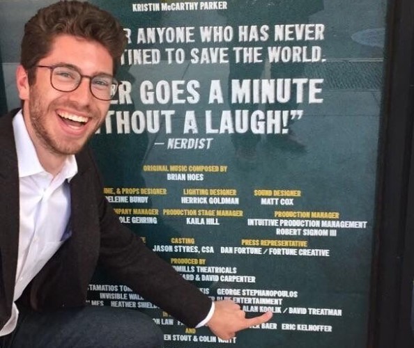 David Treatman: A bespectacled man smiling broadly, pointing his finger at a poster.