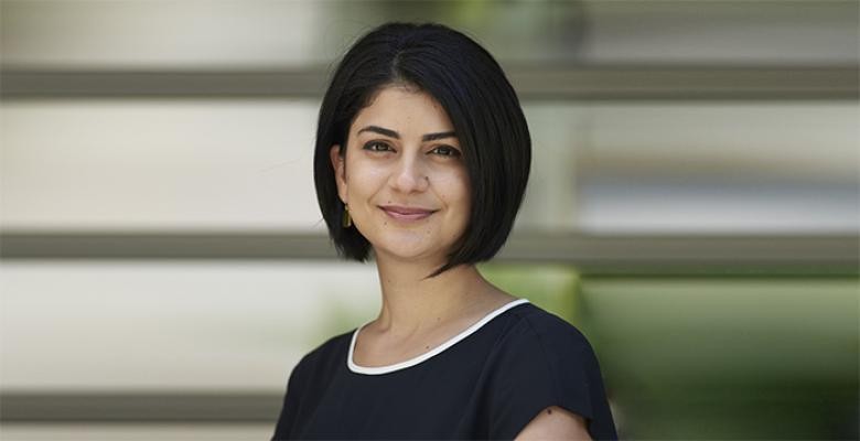 Turkuler Isiksel dressed in a black dress with crew neck trimmed in white. Dark hair cropped to a bob. Smiling directly into camea lens.