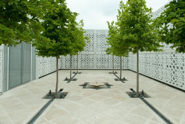 Green trees on mosaic tiled ground surrounding a fountain.