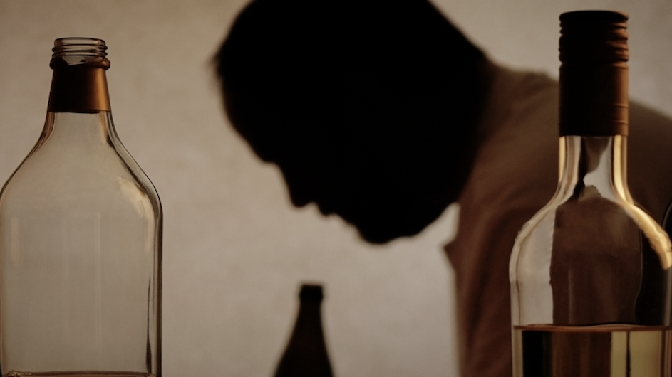 A man in silhouette behind bottles of alcohol.