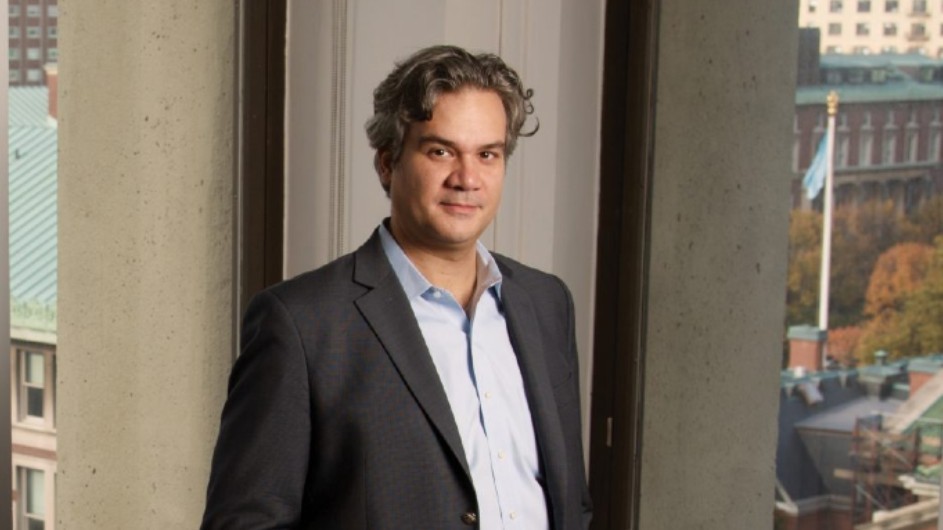 A white man standing in front of windows and walls