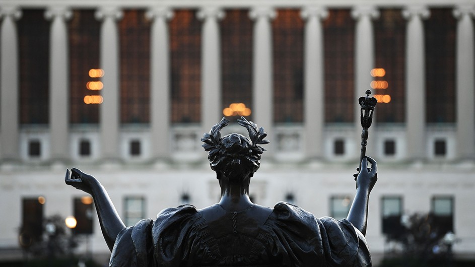 The shoulders of Columbia's Alma Mater statue are seen from behind with Butler Library in the distance.