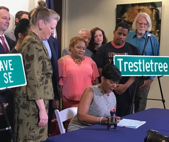 An African American woman is seated signing at the desk surrounded by people with street signs next to her.