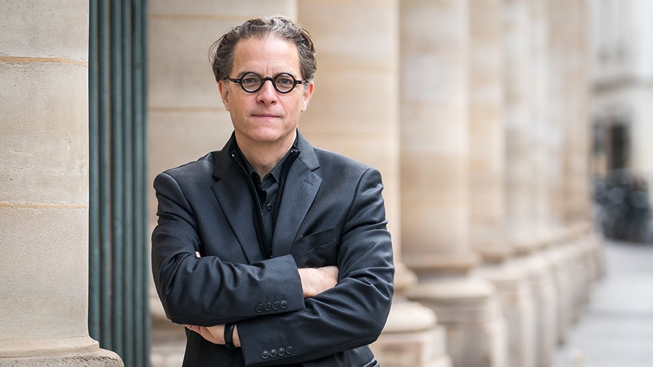 Bernard E. Harcourt: A man with eyeglasses and crossed arms poses near a row of stone building columns.