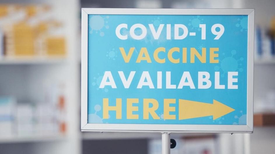 A sign that says "COVID-19 Vaccine Available Here," with an arrow pointing to the right.