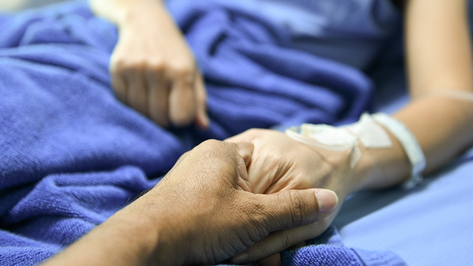 A visitor holds the hand of a patient lying in bed