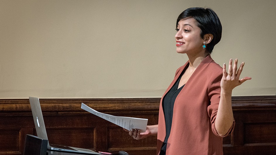 Debashree Mukherjee: A woman with short dark hair smiles and lectures while standing in front of an open laptop.