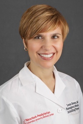 Female-presenting person with blonde hair, in lab coat, smiling. 