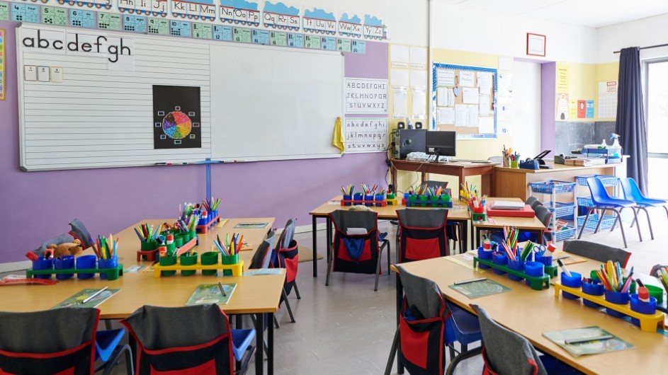 Empty elementary school classroom with tables, chairs and containers of colorful pencils.