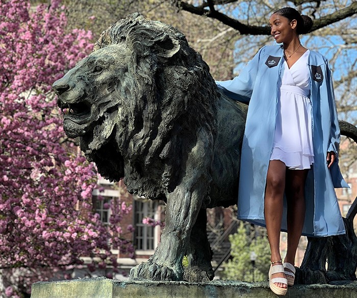 A student in Commencement regalia poses with Scholar's Lion