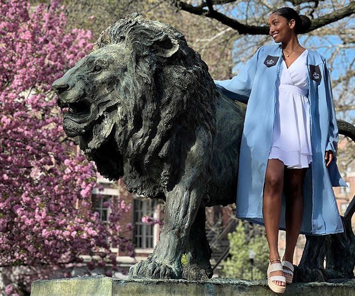 Photo courtesy Jade Durand (GSAPP'23). A student in Commencement regalia poses with Scholar's Lion