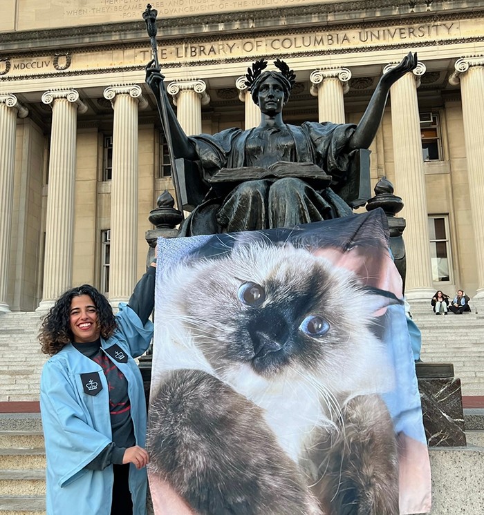A student holds a gigantic picture of her cat in front of Alma Mater. 