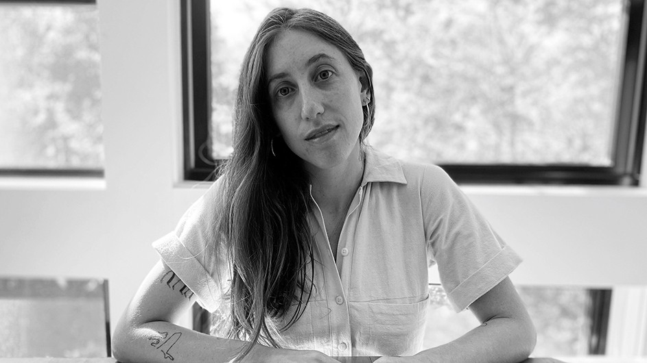 A woman with long hair and wearing a shortsleeved white shirt looks into the camera.