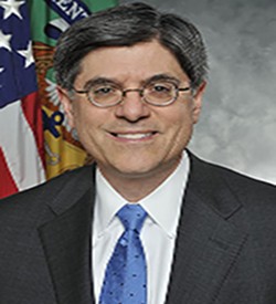 jacob lew dressed in a dark blazer with a royal blue tie with polka dots and white shirt.  Adorning wired rimmed eyeglasses with an American and a Treasury Dept flag in the rear