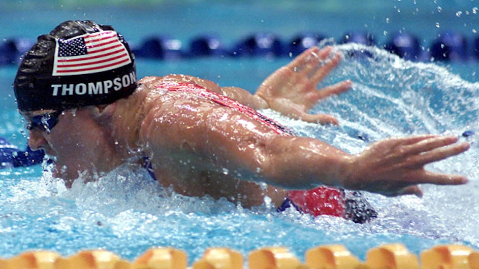 An action shot of olympic swimmer Jenny Thompson in the pool wearing a swim cap with the U.S. flag on it